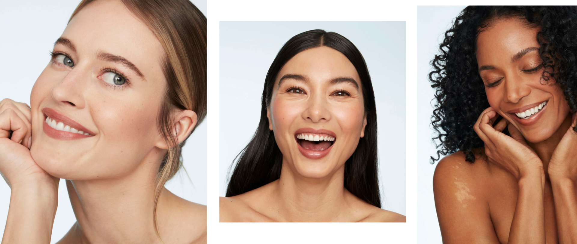 Three women with different skin tones and hair types smiling against a light background, photographed from the shoulders up.